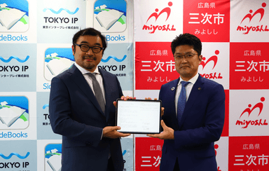 協定書(タブレット端末)を掲げる 三次市 福岡 誠志 市長(右)と東京IP 代表取締役 米田 英輝