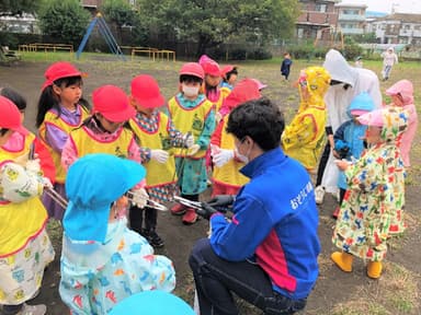 清掃場所の公園でゴミを拾うトングを渡して説明するスタッフ