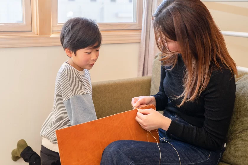 母がランドセルのフタを手縫いしている様子。